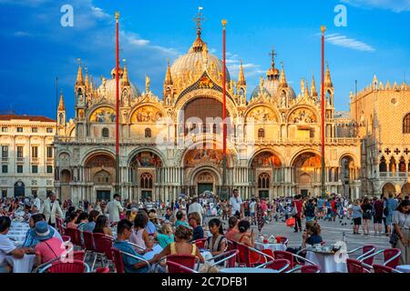 Basílica de San Marco reflejado en acqua alta en la Piazza San Marco al atardecer, Venecia, Italia con movimiento desenfocado en las multitudes de turistas