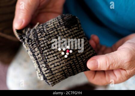 Almohadilla blanda para agujas de coser. Las manos de ancianos de un costurero sostienen una herramienta. Vista desde arriba. Foto de stock