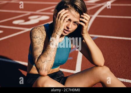 Hermosa chica atleta húmeda en sportswear sensualmente mirando en la cámara mientras descansa después de correr en el estadio de la ciudad Foto de stock