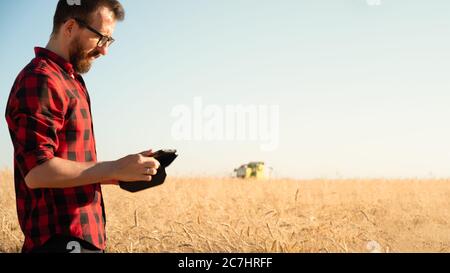 Retrato de un hombre con tablilla un campo de trigo o centeno. Agricultor moderno, gestión de negocios agrícolas, concepto de propietario de negocios locales Foto de stock