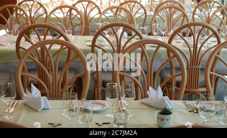 Enfoque selectivo de mesas cubiertas de cubiertos y rodeadas por sillas de madera Foto de stock