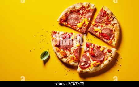 Pizza sazonada picante o de pepperoni en rodajas con pimientos en amarillo con copyspace visto como una cama plana desde arriba Foto de stock