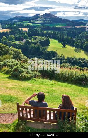 una pareja sentada en un banco de madera disfrutando de la vista panorámica conocida Como "Scott's View" en la colina de Bemersyde cerca de Melrose en el Fronteras escocesas Foto de stock
