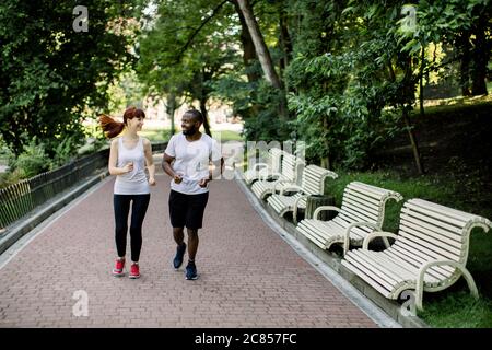 Feliz joven feliz pareja multiétnica, afroamericano y mujer caucásica, jogging a través del callejón del parque de la ciudad a primera hora de la mañana con el amanecer y.