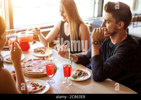 Concepto de pizza y comida en la calle. Feliz joven sonriente pareja interracial pasar tiempo junto con amigos en el café, comer pizza.