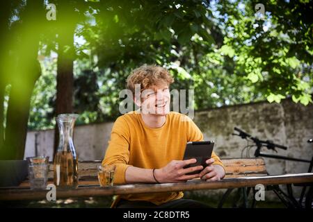 Retrato de un joven sentado en la mesa de la cerveza en el jardín con tableta digital