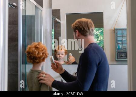 Lindo chico mirando el espejo reflejo de su padre cepillándose pelo en el baño