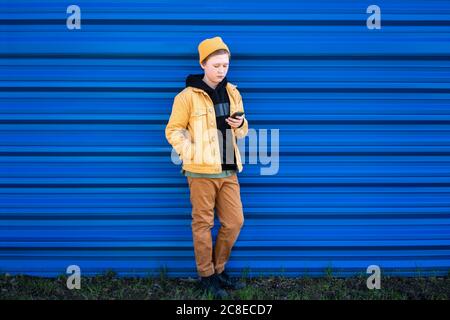 Niño usando el teléfono inteligente mientras está de pie contra el obturador azul