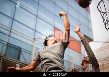dos jóvenes asiáticos jugando al baloncesto subiendo para un rebote en la cancha al aire libre Foto de stock