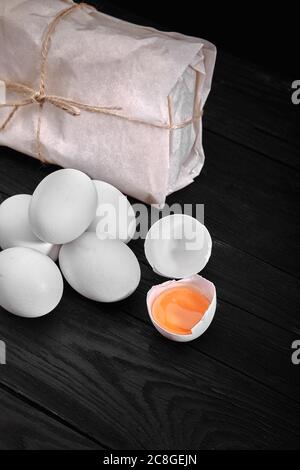 Huevos blancos de pollo frescos con heno en saco y madera rústica, agricultura orgánica sobre fondo negro. Alimentos naturales saludables