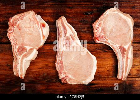 tres chuletas de cerdo crudas sobre superficie de madera Foto de stock