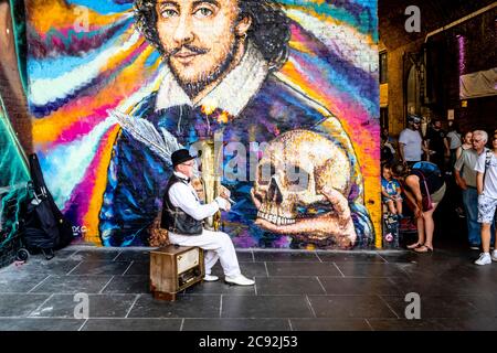 A Street Entertainer toca Música frente A UN Mural Gigante de William Shakespeare, Clink Street, Londres, Reino Unido Foto de stock