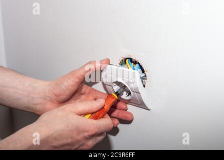 Cierre de manos de electricista reparando la toma eléctrica de pared con un destornillador. Reparación de la fijación de la caja de salida eléctrica suelta Foto de stock