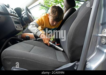 Niño haciendo la limpieza de la tapicería dentro de un coche con una aspiradora para ganar dinero de bolsillo durante las vacaciones escolares de verano Gales Reino Unido KATHY DEWITT Foto de stock