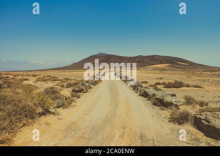 La solitaria carretera desértica a través de un paisaje árido serpentea hacia montañas volcánicas en el horizonte, vista en las llanuras de Rubicon cerca de Playa Blanca, Lanzarote. Foto de stock
