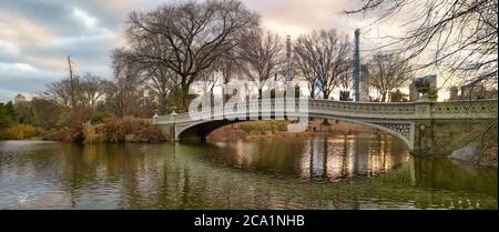 El puente de proa en el parque central, la ciudad de Nueva York luz del día vista con reflexión en el agua, las líneas del cielo, las nubes y los árboles