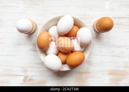 Cuenco con huevos de pollo marrón y blanco sobre mesa de madera. Huevos marrones y blancos en plato y sostenedores sobre fondo de madera. Huevos orgánicos de gama libre. Plana la