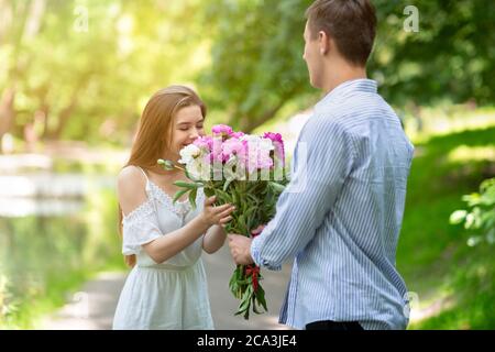 Hermosa mujer olor ramo de flores dado por su novio en el parque Foto de stock