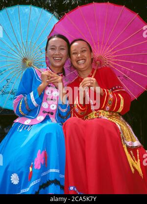 Dos Smiling joven vestida con ropa tradicional China, sosteniendo umberella en un parque, Yunnan, China Foto de stock