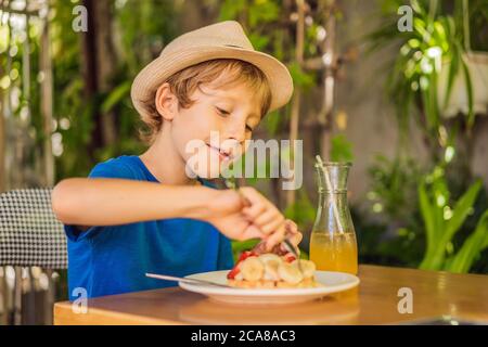 Un niño come gofres belgas de postre con fresa en una cafetería Foto de stock