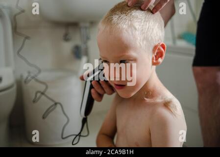 Padre haciendo corte de pelo para su hijo en casa con máquina de corte de pelo en el baño Foto de stock