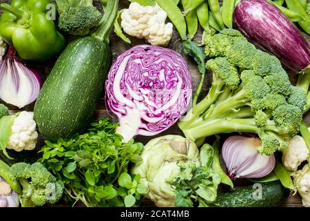 Vista superior conjunto crudo de verduras verdes, rojas y púrpuras esparcidas sobre fondo de madera oscura Foto de stock