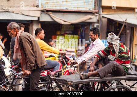 Agra / India - 22 de febrero de 2020: Viejo hombre indio sentado en la plataforma de un triciclo en la calle histórica del centro con tráfico pesado Foto de stock