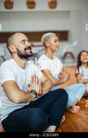 Padres jóvenes caucásicos con niño meditando en casa, sentados en el suelo. Familia, deporte, yoga concepto. Colores blancos Foto de stock