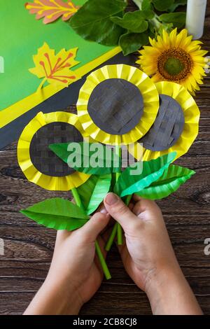 El niño sostiene girasol de flor de papel sobre una mesa de madera.  Proyecto de arte infantil, artesanal, artesanía para niños Fotografía de  stock - Alamy