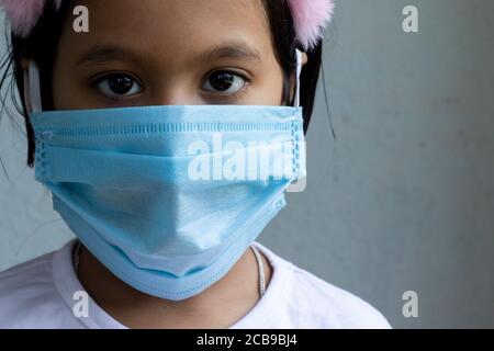 Disparo de cabeza de una niña India usando nariz quirúrgica máscara mirando la cámara para detectar el virus de la corona o la protección covid-19