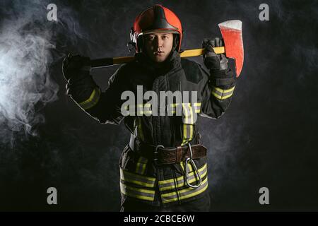 un joven bombero adulto que salva a la gente del fuego usando uniforme y  casco, sosteniendo el equipo de lucha contra incendios Fotografía de stock  - Alamy