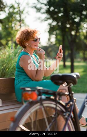 Mujer madura utilizando videollamada en su smartphone en el parque Foto de stock