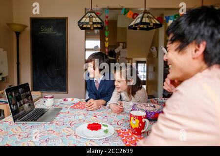 Una familia sonriente se sienta a la mesa en una reunión de zoom fiesta de cumpleaños Foto de stock