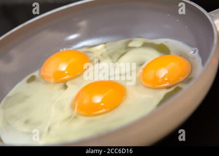 Desayuno de fondo. Tres huevos cocinados en una sartén de cerca Foto de stock