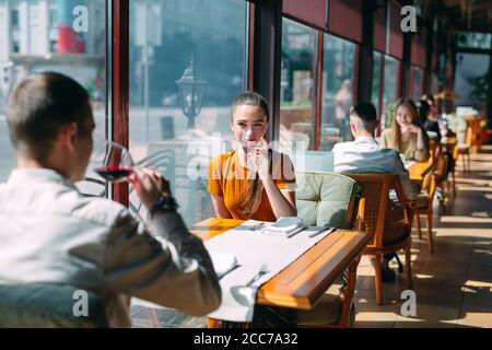 Una joven pareja bebiendo vino en un restaurante cerca de la ventana.