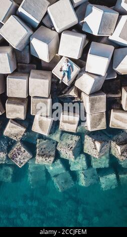 Vista aérea de un joven sobre bloques de cemento que protegen la costa de las olas del puerto de Málaga, España. Foto de stock