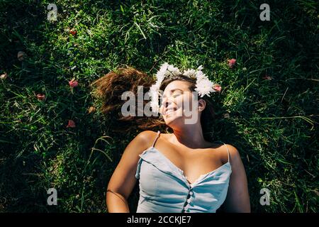 Mujer joven con los ojos cerrados relajándose en la tierra verde adentro estacione durante el día soleado Foto de stock