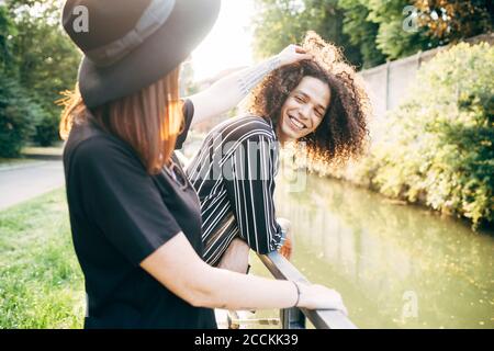Mujer joven jugando con el pelo rizado de su novio mientras está de pie estanque en el parque