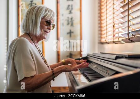 Mujer mayor con gafas de sol jugando al piano mientras se sienta en casa