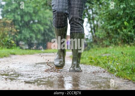 Vista frontal cercana de las botas de agua verdes que lleva al aire libre la mujer salpicando a través de charcos bajo fuertes lluvias, Reino Unido. Foto de stock