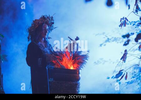 Una bruja del bosque hace una poción sosteniendo una muñeca Voodoo. Foto de stock