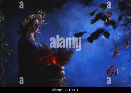 Una bruja del bosque hace una poción sosteniendo una muñeca Voodoo. Foto de stock