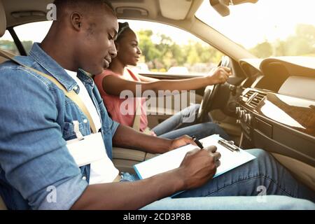 Instructor masculino que examina a la mujer negra que conduce el coche Foto de stock