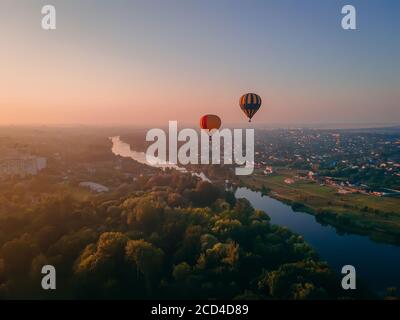 Dos globos de aire de colores volando sobre el parque verde y el río en la pequeña ciudad europea al amanecer de verano, región de Kiev, Ucrania Foto de stock