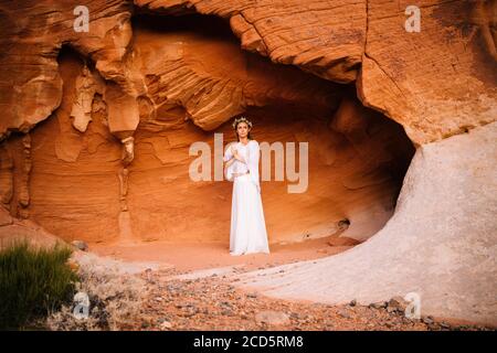 Mujer como la ninfa en blanco de pie por la formación de piedra arenisca azteca, Parque Estatal, Desierto de Mohave, Overton, Nevada, EE.UU