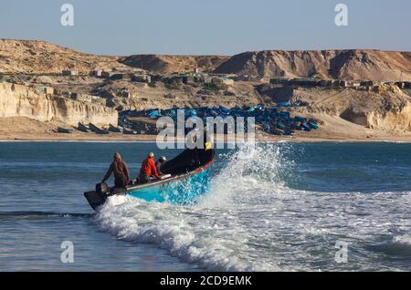 Marruecos, Sáhara Occidental, Dakhla, pescadores tomando el mar en su barco frente a la playa de Araiche bordeado por un acantilado Foto de stock