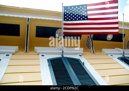 Una bandera americana, las estrellas y las rayas, colgando sobre la ventana con cierre de una escopeta amarilla, French Quarter, New Orleans, Louisiana, USA.
