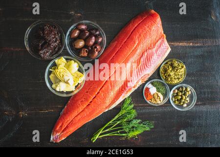 Salmón Mediterráneo Ingredientes: Filete de pescado crudo, hierbas, especias y otros ingredientes sobre un fondo de madera oscura Foto de stock