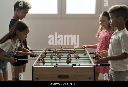 Un grupo de niños multiculturales y lindos están en el interior pasar tiempo de juego con amigos jugando al futbolín juntos. Versión de mesa de los amantes del fútbol.