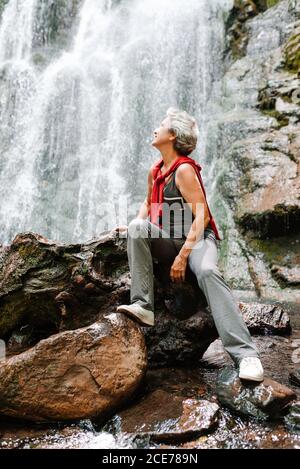 Mujer viajera de tercera edad sin preocupaciones cerca de la cascada Foto de stock